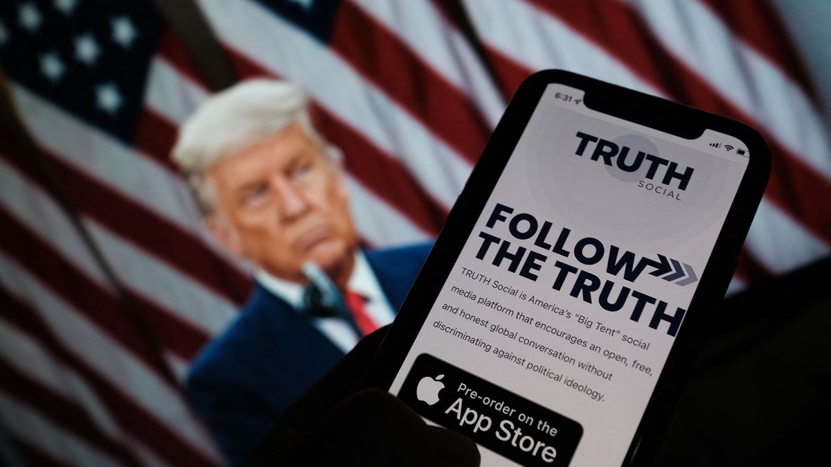 This illustration photo shows a person checking the app store on a smartphone for "Truth Social", with a photo of former US president Donald Trump on a computer screen in the background, in Los Angeles, October 20, 2021. - Former US president Donald Trump announced plans on October 20 to launch his own social networking platform called "TRUTH Social," which is expected to begin its beta launch for "invited guests" next month. The long-awaited platform will be owned by Trump Media & Technology Group (TMTG), which also intends to launch a subscription video on-demand service that will feature "non-woke" entertainment programming, the group said in a statement. (Photo by Chris DELMAS / AFP)