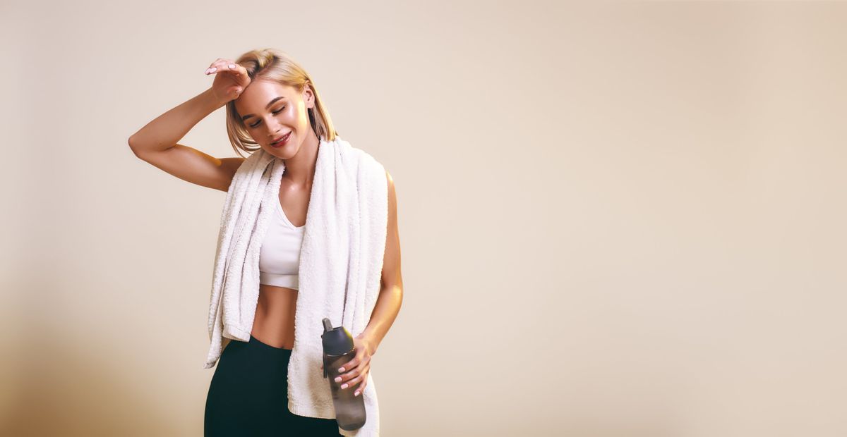 It was great workout! Cute and young sporty woman in sports clothing with towel on shoulders keeping eyes closed and smiling while standing in studio