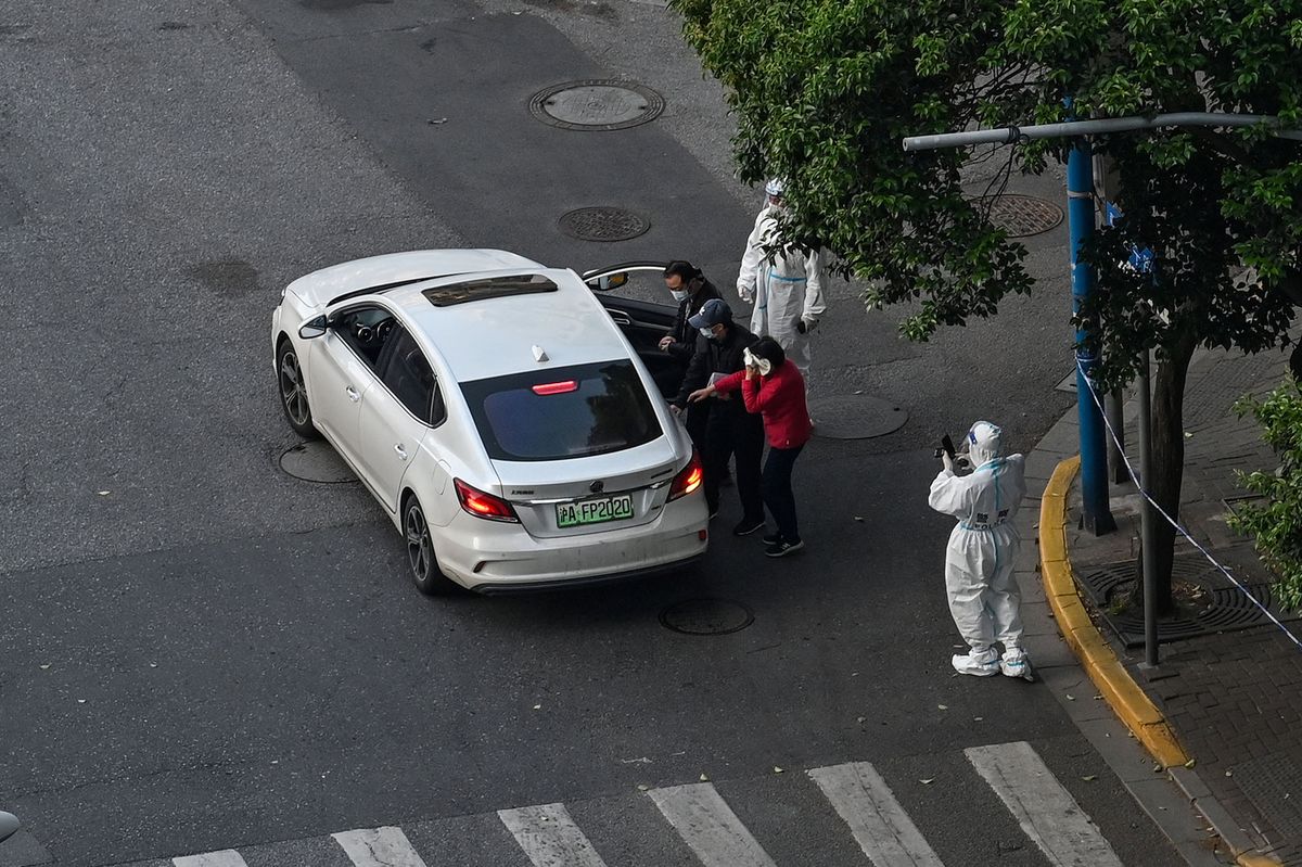 A policeman (bottom R) wearing personal protective equipment (PPE) stands on the street while residents (C) get into a car during the Covid-19 coronavirus lockdown in the Jing'an district in Shanghai on May 5, 2022. (Photo by HECTOR RETAMAL / AFP)