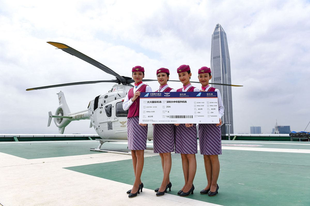 (210318) -- SHENZHEN, March 18, 2021 (Xinhua) -- Flight attendants hold a large-size air ticket at the maiden flight ceremony of a newly introduced airport helicopter shuttle service on a helipad in downtown Shenzhen, south China's Guangdong Province, March 18, 2021.  The Shenzhen civil aviation authority on Thursday launched a helicopter shuttle service between Shenzhen Bao'an International Airport and Futian District, the city's central business district. The flight route passes many urban landmarks of Shenzhen, and travel time can be as short as 10 minutes. At present, the service is provided only to passengers arriving from Beijing Daxing International Airport. (Xinhua/Mao Siqian) (Photo by Mao Siqian / XINHUA / Xinhua via AFP)