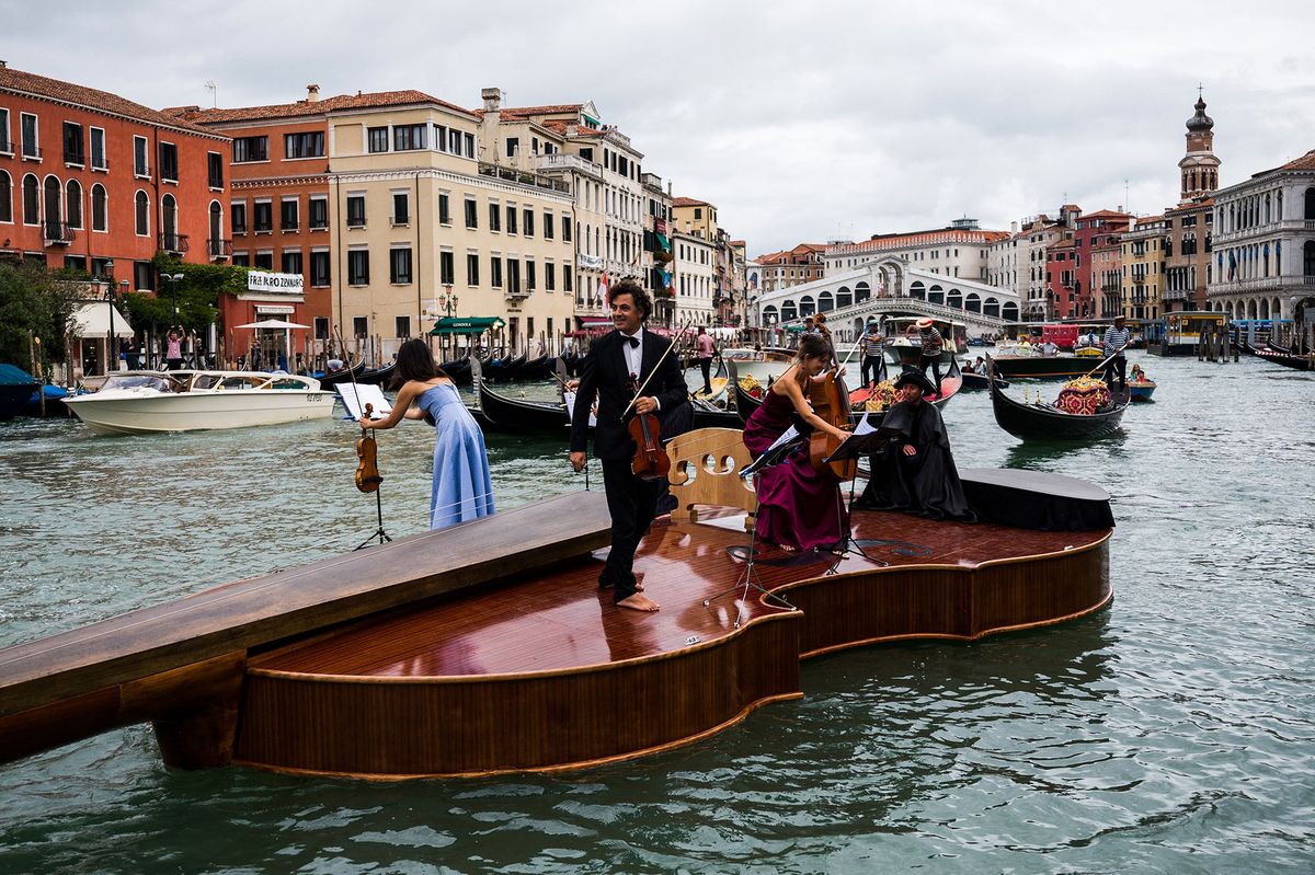 Musicians stand on "Noah's Violin", a giant floating violin by Venetian sculptor Livio De Marchi, as it makes its maiden voyage for a concert on the Grand Canal near the Rialto bridge in Venice on September 18, 2021. - Twelve and a half metres of wood, some of it hand-crafted, symbolizing the rebirth of Venice through art, culture and music, said the authors. The floating violin is hosting musicians from the Benedetto Marcello Conservatory playing Vivaldi. (Photo by Marco BERTORELLO / AFP)