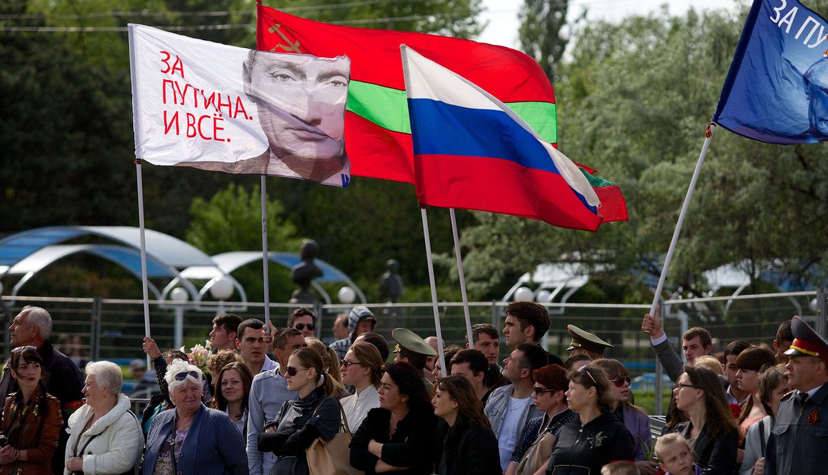 People carry a Russian flag (C) and a flag with a portait of  Russia's President Vladimir Putin reading "We are for Putin!"  in Tiraspol, the main city of Transdniestr separatist republic of Moldova, on May 9, 2014, during Victory Day celebrations. Transnistria, a small strip of land of 500,000 inhabitants in eastern Moldova, has won the support of Russia, a short war of independence after the collapse of the USSR in 1991. It is not recognized by the international community. AFP PHOTO/ VADIM DENISOV (Photo by VADIM DENISOV / AFP)