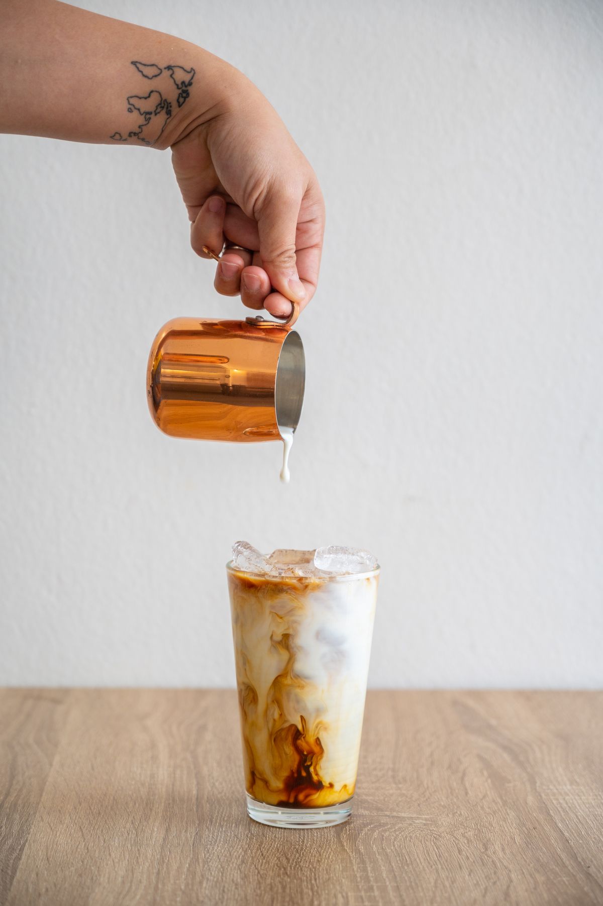 Barista hand pouring milk into an iced coffee for making iced latte.