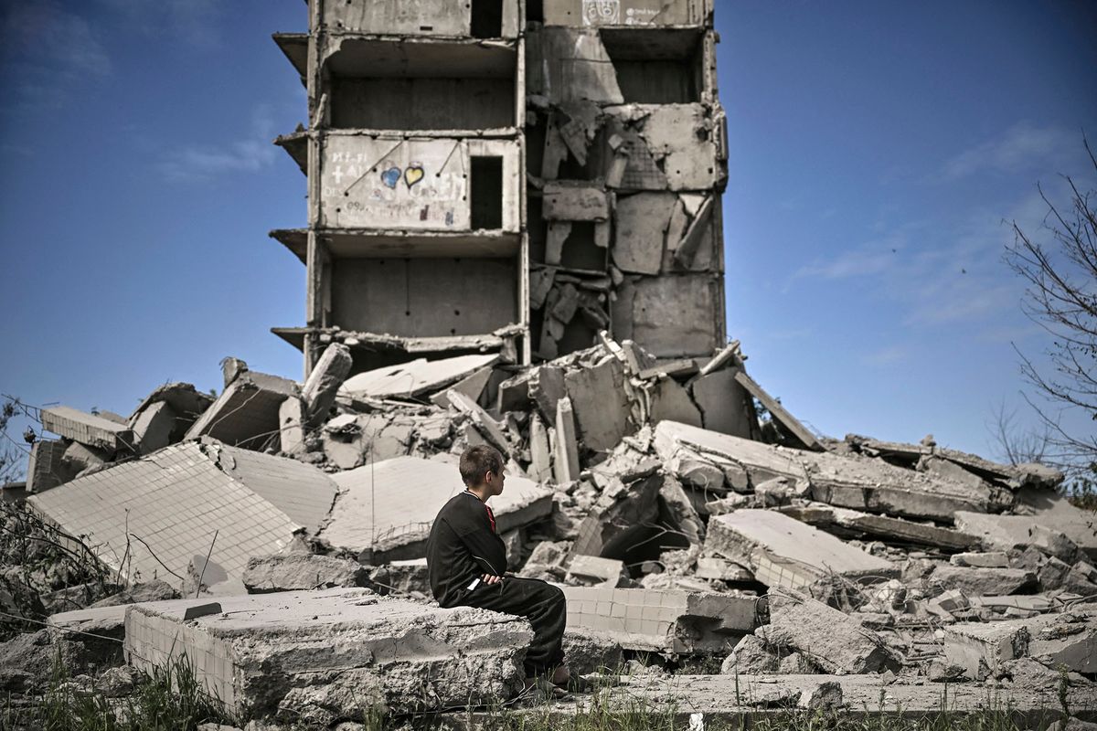 A young boy sits in front of a damaged building after a strike in Kramatorsk in the eastern Ukranian region of Donbas, on May 25, 2022. (Photo by ARIS MESSINIS / AFP)