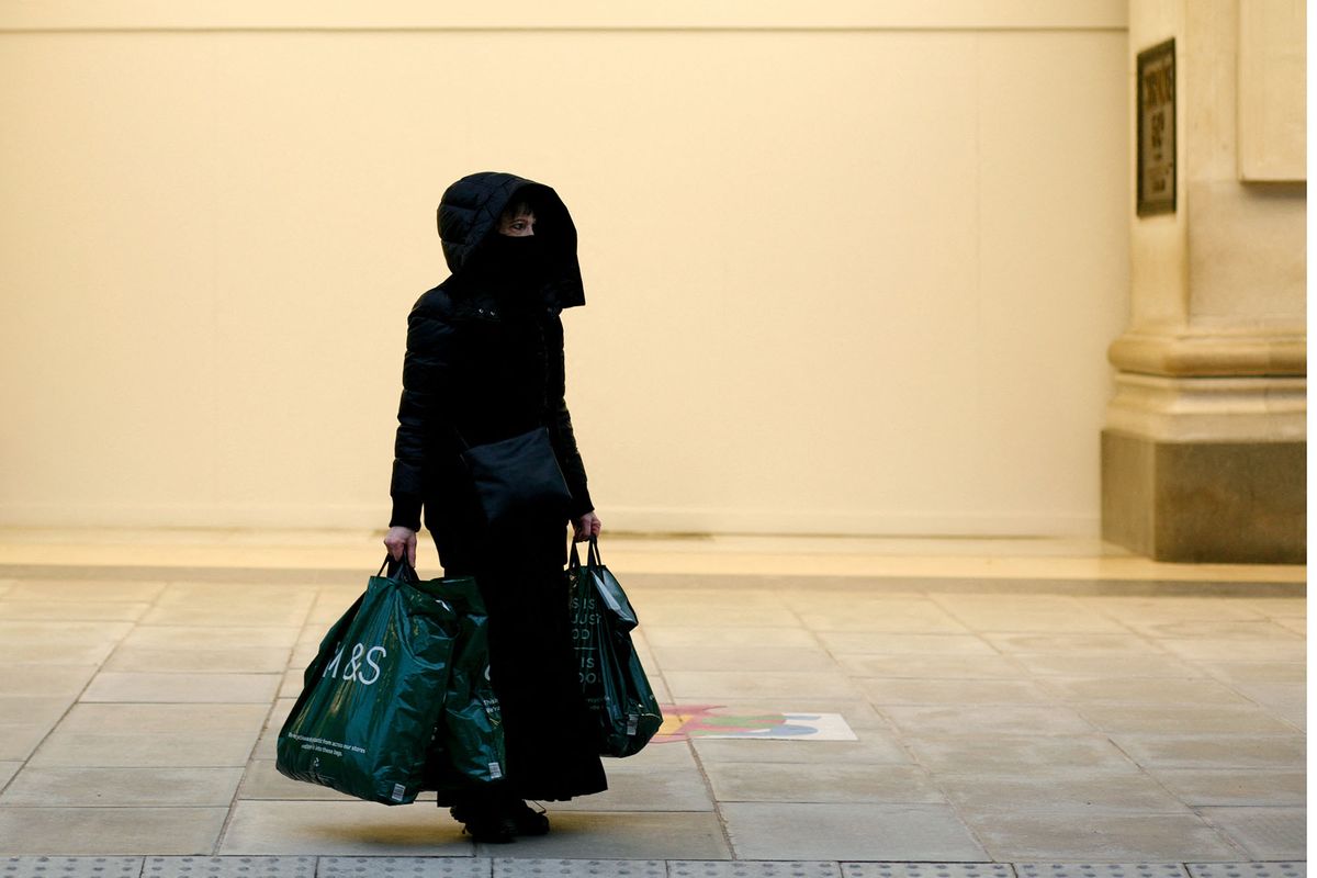 A woman wearing a face mask carries bags from food and clothing retailer Marks and Spencer outside the boarded-up entrance of temporarily-closed department store Selfridges on Oxford Street in London, England, on March 11, 2021. This week marked the first stage of coronavirus lockdown easing across England, with schools reopening and some limits on social contact loosened. Non-essential shops, bars, restaurants and other hospitality and leisure businesses remain closed, however, and will not reopen until next month under the current timetable. (Photo by David Cliff/NurPhoto) (Photo by David Cliff / NurPhoto / NurPhoto via AFP)