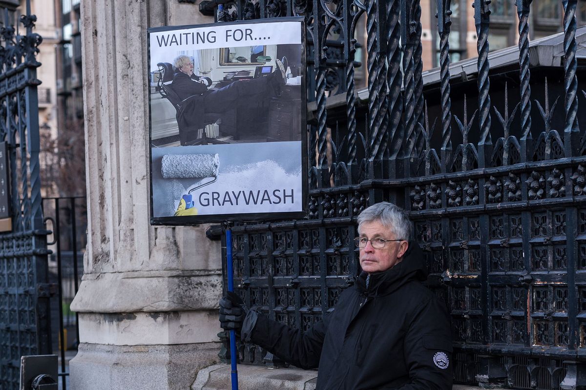 LONDON, UNITED KINGDOM - JANUARY 19, 2022: A demonstrator holds a placard reading 'Waiting for Graywash' refering to Sue Gray's investigation into alleged parties in Downing Street outside Houses of Parliament on January 19, 2022 in London, England. A senior civil servant Sue Gray is currently conducting an investigation into several alleged lockdown rule-breaking parties in Downing Street as Boris Johnson denied being warned that the garden party on 20 May 2020 could be against Covid-19 rules in place at the time. (Photo by WIktor Szymanowicz/NurPhoto) (Photo by WIktor Szymanowicz / NurPhoto / NurPhoto via AFP)