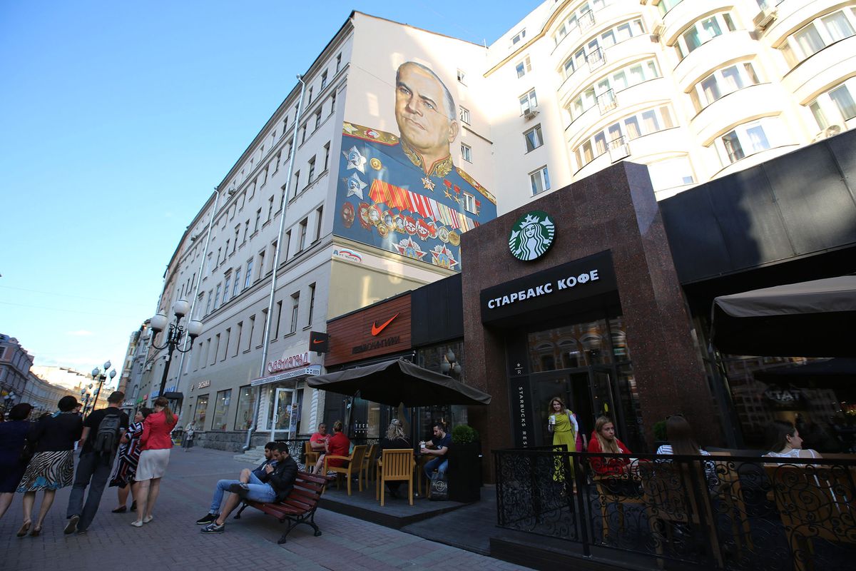 476430804 A wall mural, depicting Russian General Georgy Zhukov, a World War II Soviet hero, sits on a building above a Nike Inc. sportswear store and a Starbucks Corp. coffee shop on Arbat street in Moscow, Russia, on Monday, June 8, 2015. Rents in Moscow's most coveted neighborhoods are plunging as demand withers with the exodus of U.S. and European executives. Photographer: Andrey Rudakov/Bloomberg via Getty Images