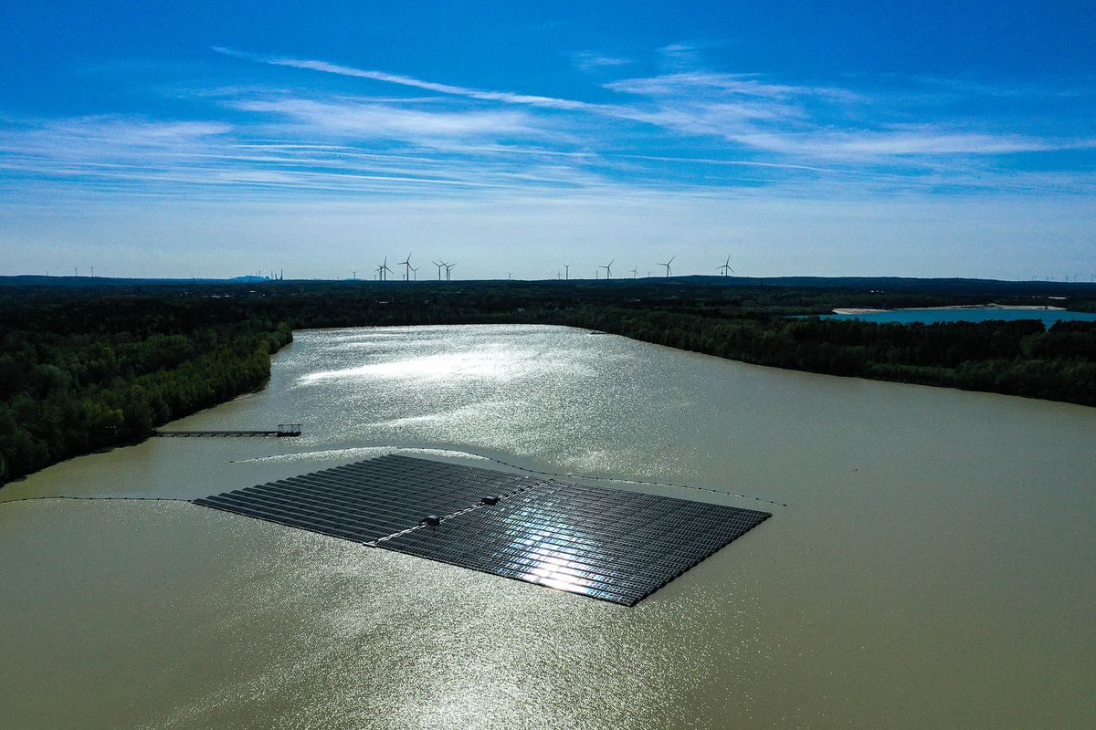 An aerial view shows solar panels at a floating photovoltaic plant on the Silbersee lake in Haltern, western Germany, with wind turbines in the distance on April 22, 2022. - Germany's largest floating solar park is currently being built and will produce almost three million kilowatt hours of electricity per year. (Photo by Ina FASSBENDER / AFP)