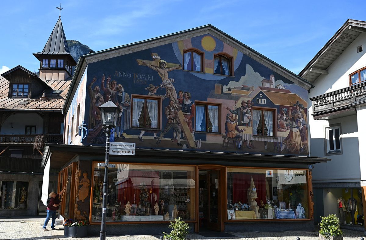 A woman cleans the store windows of a painted house in Oberammergau, southern Germany, the village hosting the traditional Passion play, on May 10, 2022. - The Oberammergau Passion play, first staged in 1634 to ward off a plague epidemic, has been staged every ten years since then, with few interruptions. The play, which brings together some 1.800 villagers who act, build, produce, or play music will run with the premiere from this Saturday, May 14 to October 2, 2022. (Photo by Christof STACHE / AFP)