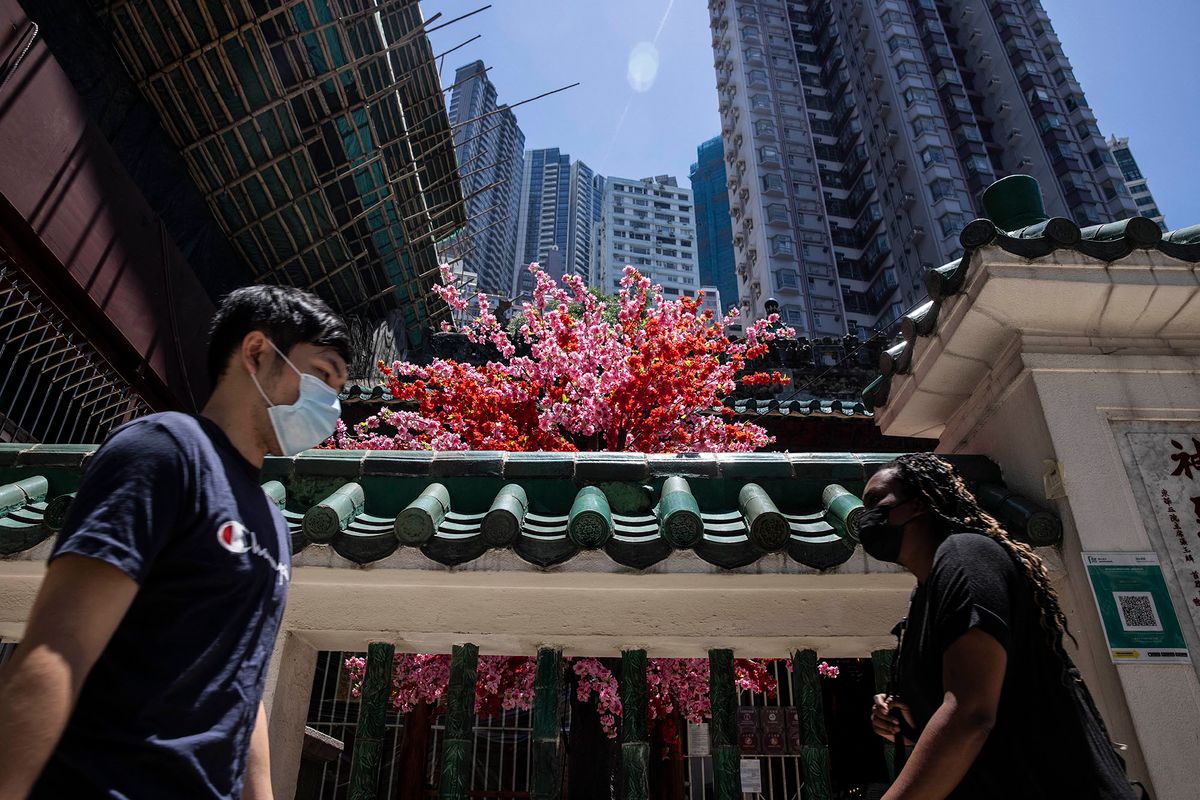 People walk past a temple in Hong Kong on May 19, 2022. (Photo by ISAAC LAWRENCE / AFP)