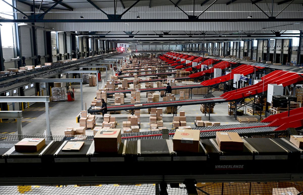 Employees work on a parcel sorting chain during a visit of Prisme, an interprofessional book distribution platform of the Geodis group in the Paris suburb of Ris-Orangis, on May 10, 2022. - The new platform, which opened in April 2022, features a sorting chain on an area of 10,000 square meters and has a capacity of 10,000 parcels per hour to sort, consolidate and distribute 7 million parcels of books annually intended for nearly 3,000 sales points in France, Belgium and Luxembourg. The platform is distributing some 67,000 tons of books per year, some 140 million books, a third of all the books for the French market. (Photo by Emmanuel DUNAND / AFP)