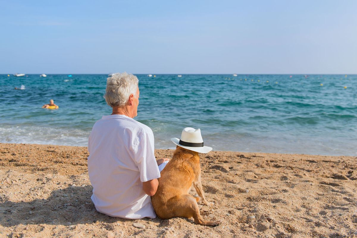 Senior man with dog in white suit sitting at the beach 