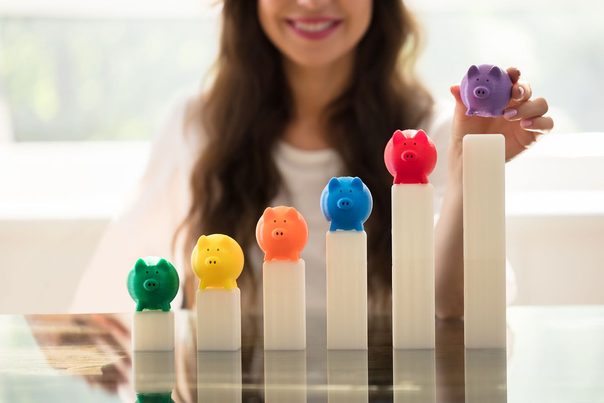 hitelállomány lakossági Businesswoman's Hand Placing Multi Colored színes malacpersely Piggybank On Growing Graph In Office