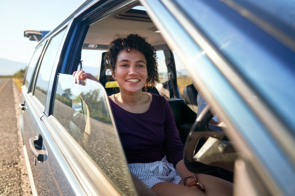 Happy young woman enjoying road trip inside car