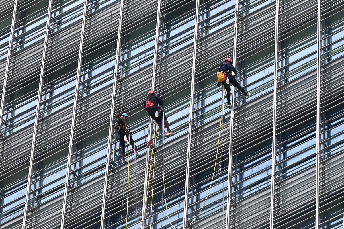 Workers secured with safety harness clean an office building facade in Singapore on September 14, 2021. (Photo by Roslan RAHMAN / AFP)
