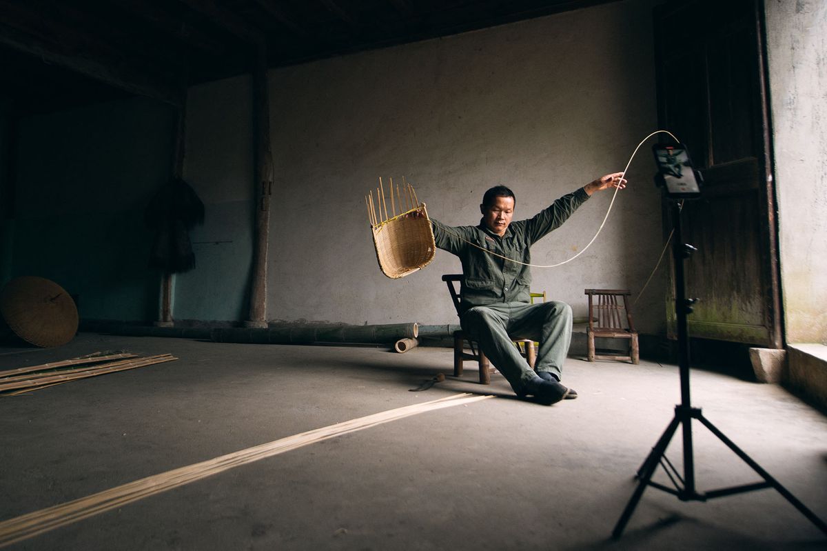 (211105) -- HANGZHOU, Nov. 5, 2021 (Xinhua) -- Pan Yunfeng shoots a video of him making a bamboo product at Hengling Village in Lin'an District of Hangzhou, east China's Zhejiang Province, Nov. 2, 2021.  A bamboo weaver in Hangzhou has amazed netizens after short videos of him turning thick bamboo into delicate slices were uploaded on social media platforms including TikTok.   Pan Yunfeng, 51, makes pot brush, baskets, umbrellas and even bathtubs out of bamboo on TikTok. He started learning bamboo weaving at an early age and began to publish his works in 2019.   With over 4.5 million followers on Douyin (the Chinese version of TikTok) and the most popular video garnering about 2 million likes, Pan has become a genuine influencer for netizens by promoting the traditional art simply using his own bare hands.  Carrying a history of 2,000 years, bamboo weaving art was listed as a national intangible cultural heritage in 2008. "Bamboo weaving has become an integral part of my life. I will work my best to preserve and pass on the craft," Pan said. (Xinhua/Jiang Han) (Photo by Jiang Han / XINHUA / Xinhua via AFP)