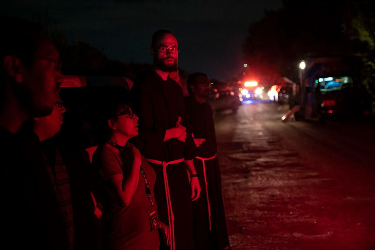 Local priests from the San Antonio Archdiocese stand near the scene where a tractor-trailer was discovered with migrants inside outside San Antonio, Texas on June 27, 2022. - At least 46 migrants were found dead June 27, 2022 in and around a tractor-trailer that was abandoned on the roadside on the outskirts of the Texas city of San Antonio. (Photo by Sergio FLORES / AFP)