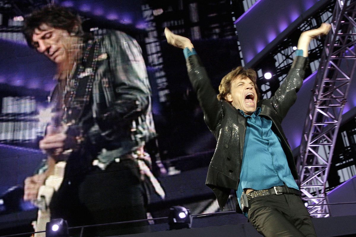 Mick Jagger (R) and Ron Wood (L, seen on screen) of the Rolling Stones performs on the stage at the Olympic Stadium during a concert in Lausanne, 11 August 2007. The only Swiss concert during the world tour of the legendary British rockers called "A Bigger Bang Tour" was organized by Switzerland's largest supermarket chain and free tickets were distributed through a lottery to holders of the chainís customer card.    AFP PHOTO / FABRICE COFFRINI (Photo by FABRICE COFFRINI / AFP)