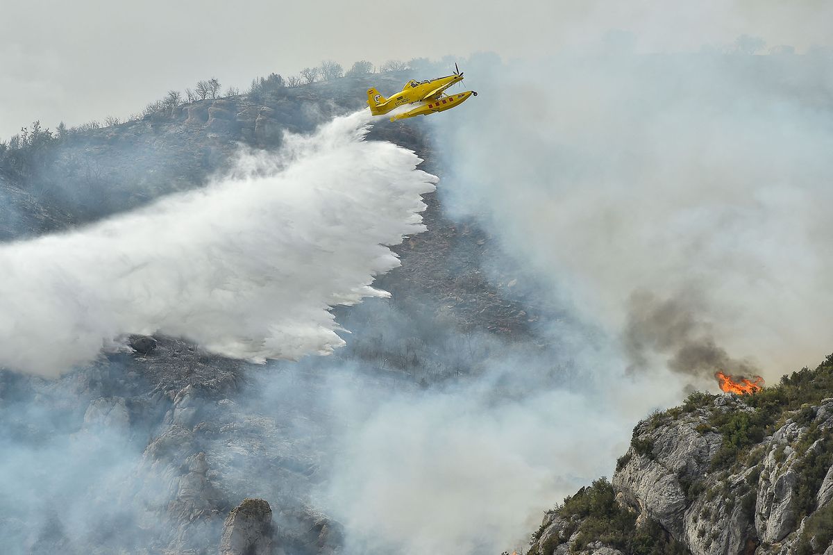 An Air Tractor AT-802A firefighting plane drops water during fire containment operations near Artesa de Segre, in Catalonia on June 16, 2022. - Emergency services battled several wildfires as Spain remained in the grip of an exceptional heatwave that has seen temperatures reach 43 degrees Celsius (109 degrees Farenheit). The most alarming blaze, near Baldomar in Catalonia, has already destroyed 500 hectares of forest but could spread to over 20,000, the government in the northwestern region said. (Photo by Pau BARRENA / AFP)
