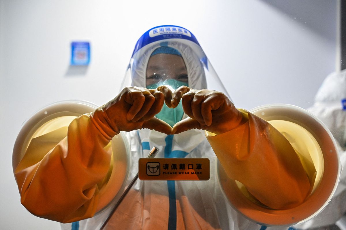 A health worker makes a heart with her hands while waiting to take swab samples from people in the Jing' an district of Shanghai on May 31, 2022, as the city prepares to lift more curbs after two months of heavy-handed restrictions. (Photo by Hector RETAMAL / AFP)