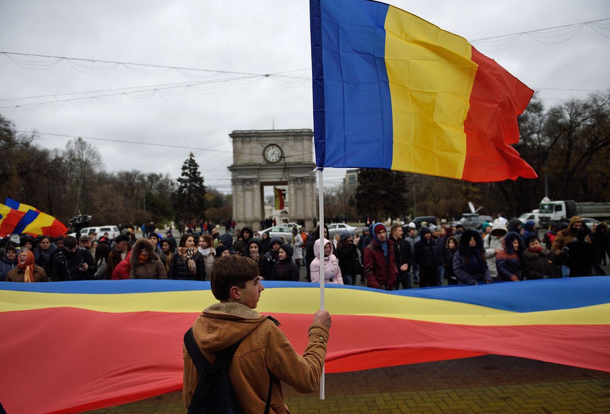 A man waves a Moldovan flag next to others holding a giant Moldovan flag during a protest in downtown Chisinau against what they consider to be a poorly organised presidential election and fraud while demanding the rescheduling of the presidential poll and the dismissal of the Central Electoral Commission (CEC) on November 14, 2016. - Pro-Russian candidate Igor Dodon emerged as winner of Moldova's presidential runoff, viewed as an East-West choice in the impoverished ex-Soviet country. With 99.9 percent of ballots counted, Socialist Party chief Dodon had 52.3 percent of the votes, according to the electoral commission, with pro-European rival Maia Sandu on 47.7 percent. (Photo by DANIEL MIHAILESCU / AFP)