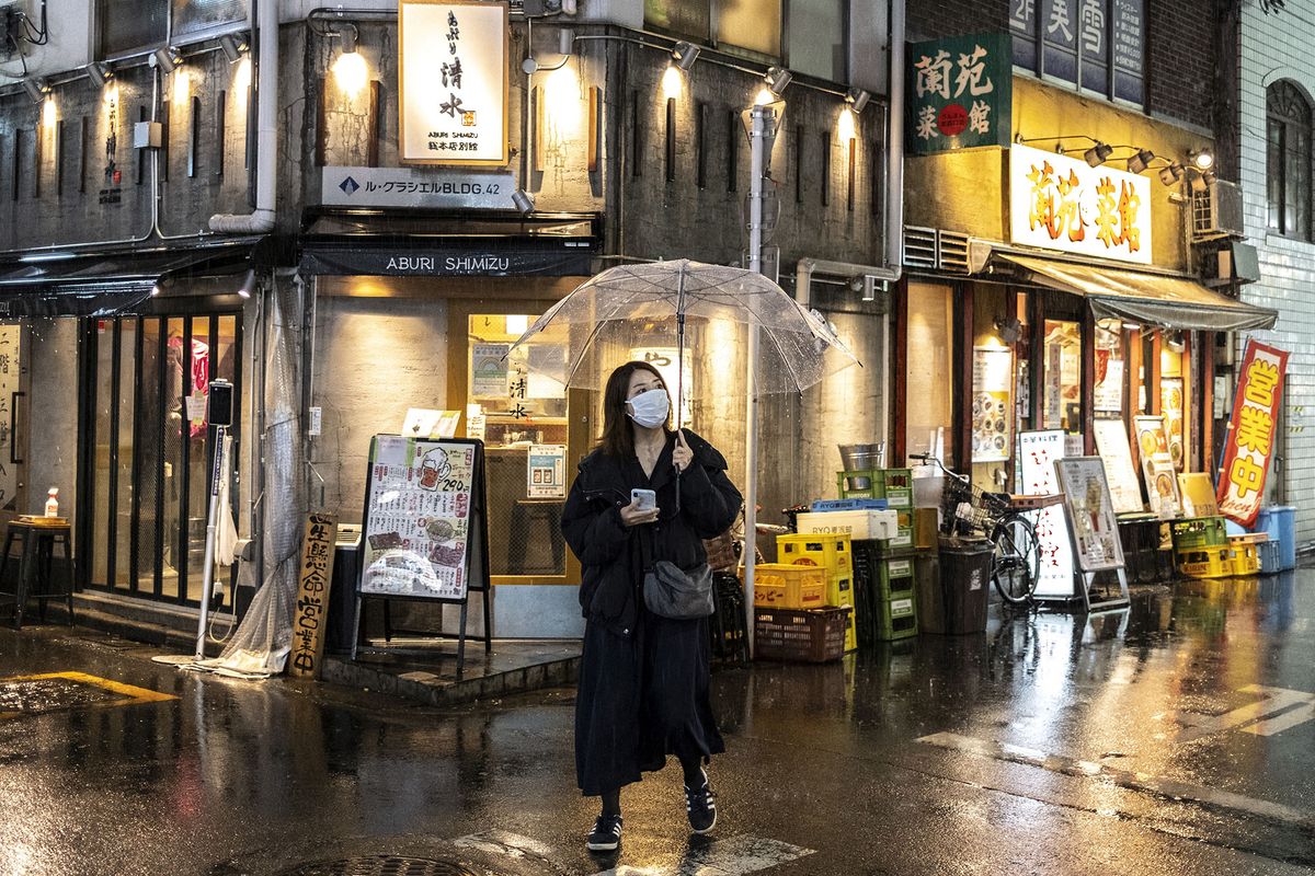 A woman walks along a street as evening rain falls in Tokyo on April 18, 2022. (Photo by CHARLY TRIBALLEAU / AFP)