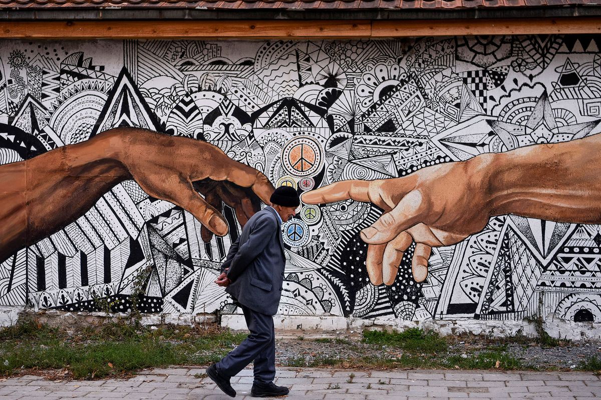 A pedestrian walks past a mural artwork painted on the wall of a house in the town of Ferizaj on November 3, 2019. (Photo by Armend NIMANI / AFP) / RESTRICTED TO EDITORIAL USE  - TO ILLUSTRATE THE EVENT AS SPECIFIED IN THE CAPTION