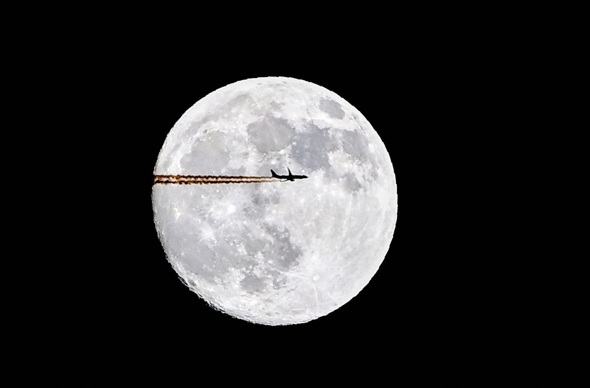 The silhouette of an airplane is seen in front of the moon in Moscow on December 28, 2020. (Photo by Yuri KADOBNOV / AFP)
