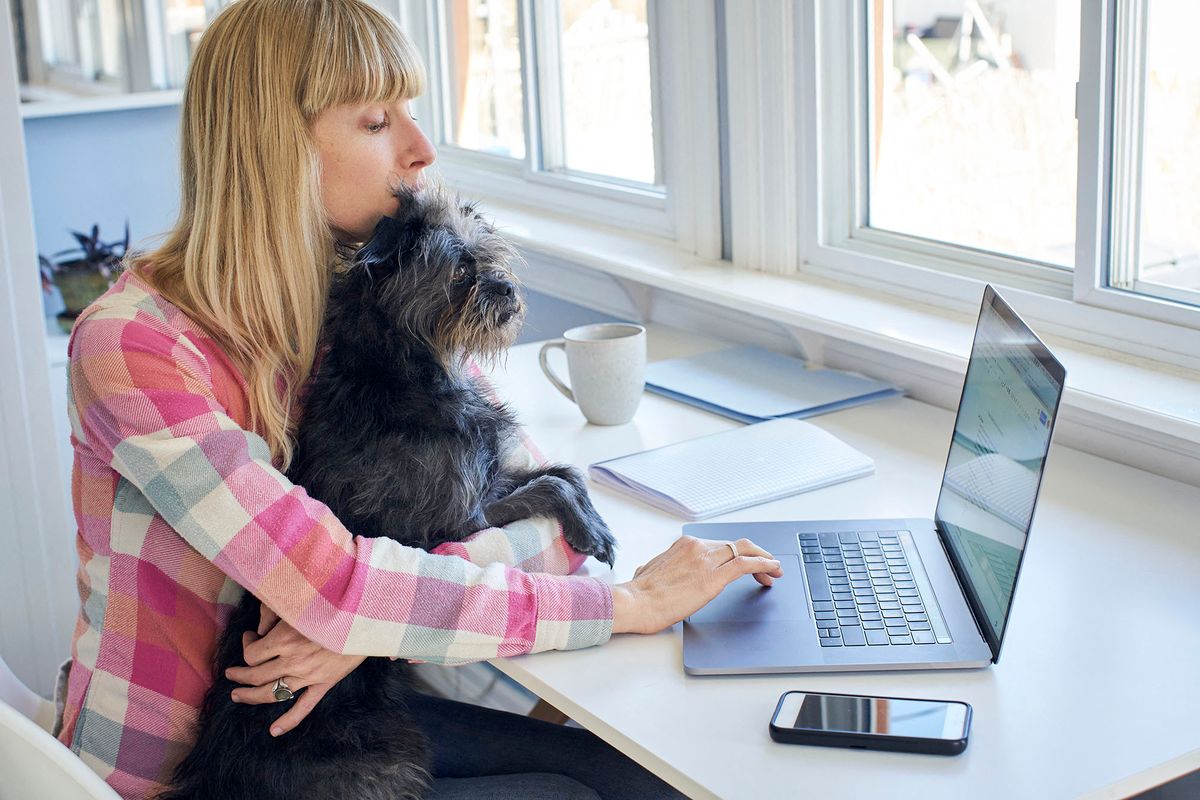 Mature woman holding dog and working from home (Photo by heshphoto / Image Source / Image Source via AFP)