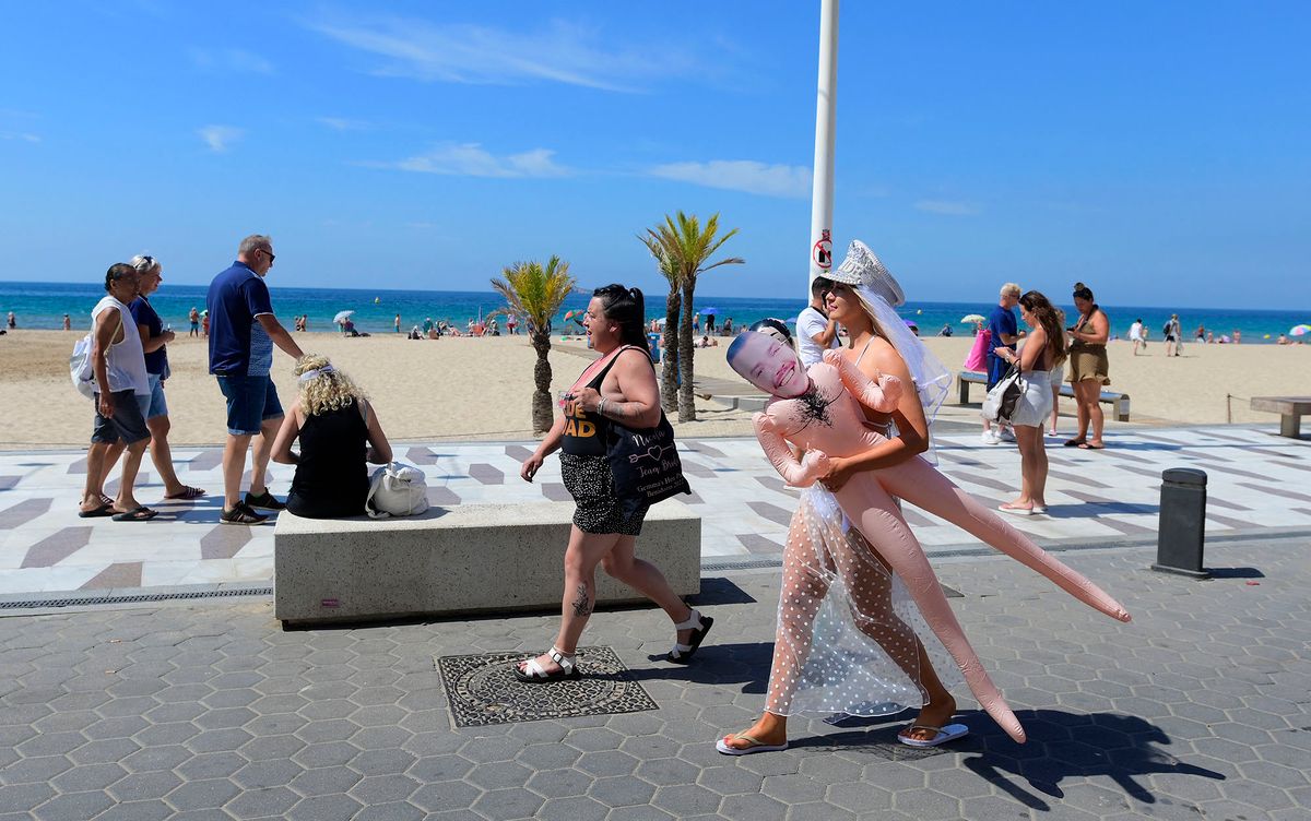 A woman carries an inflatable dummy as she walks along the promenade at Levante Beach in Benidorm on June 7, 2022. - Whether it's chefs, bar staff or dishwashers, many bars, restaurants and cafes across Benidorm are struggling to recruit workers, generating a new source of tension after two years of pandemic. (Photo by JOSE JORDAN / AFP)