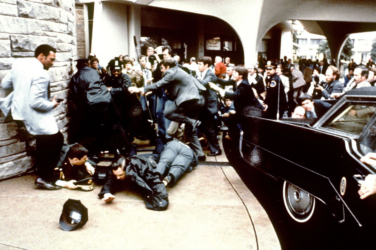 (FILES) In this file photo taken on March 30, 1981 this photo taken by presidential photographer Mike Evens on March 30, 1981 shows police and Secret Service agents reacting during the assassination attempt on then US president Ronald Reagan, after a conference outside the Hilton Hotel in Washington, DC. Reagan was hit by one of six shots fired by John Hinckley, who also seriously injured press secretary James Brady (just behind the car).  Reagan was hit in the chest and was hospitalized for 12 days. Hinckley was aquitted 21 June 1982 after a jury found him mentally unstable. - John Hinckley, who attempted to assassinate US president Ronald Reagan in 1981, was granted unconditional release June 1, 2022 by a Washington judge, six years after he was freed from a psychiatric hospital. (Photo by Mike Evens / CONSOLIDATED NEWS PICTURES / AFP)