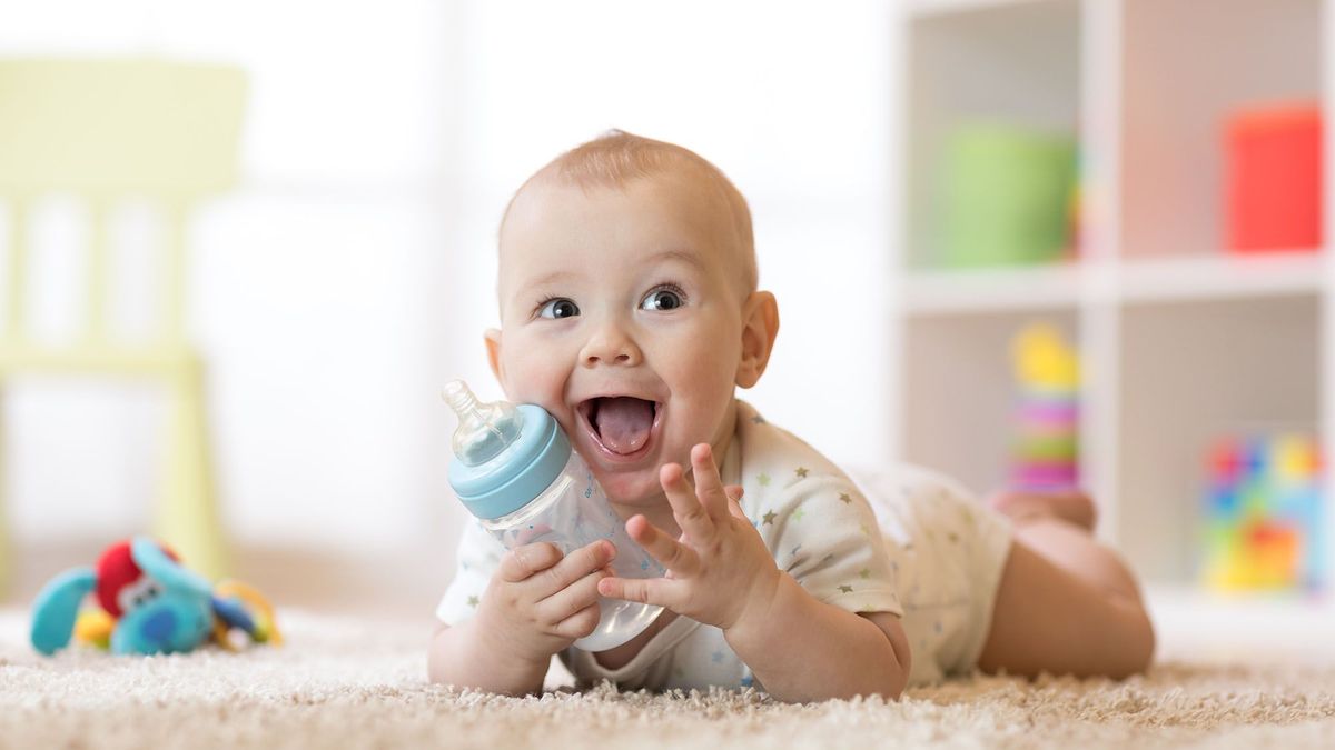 csecsemő tápszerek Cute baby boy drinking from bottle. Kid lying on carpet in nursery at home. Smiling child is 7 months old.