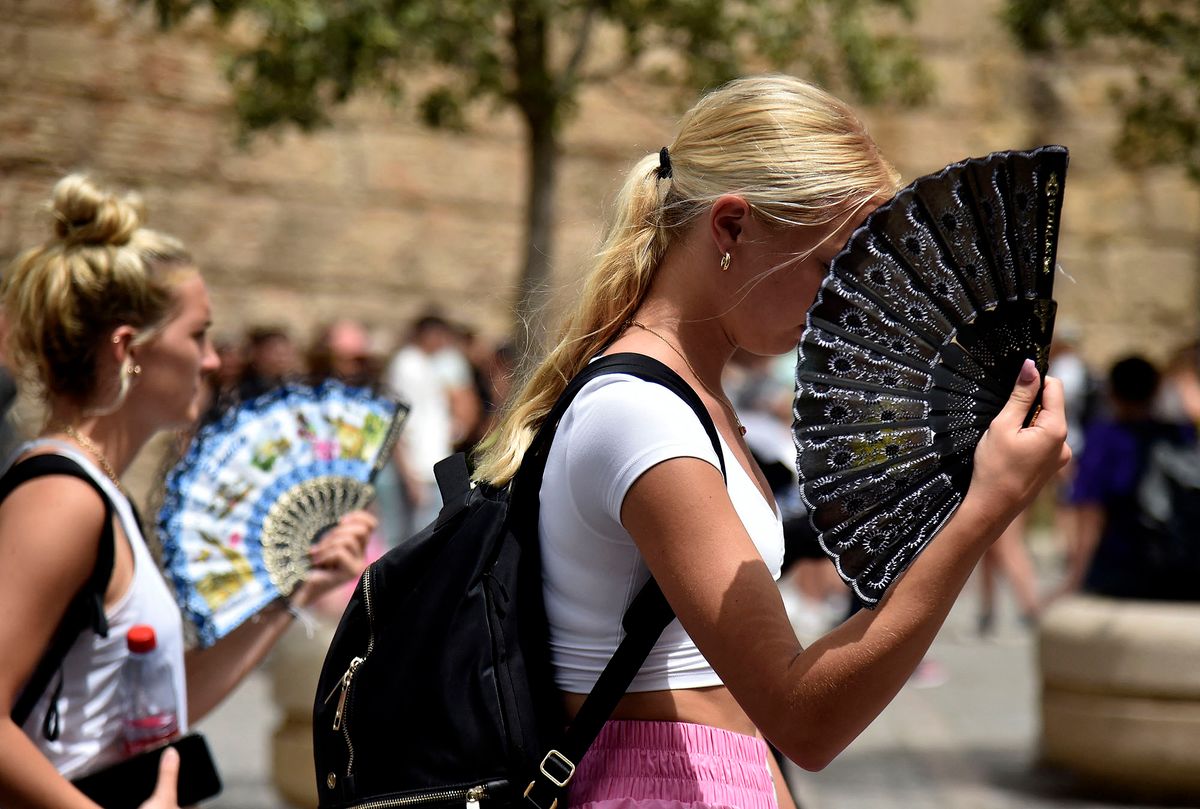 Two women use fans to fight the scorching heat during a heatwave in Seville on June 13, 2022. - Spain was today already in the grips of a heatwave expected to reach "extreme" levels, and France is bracing for one, too, as meteorologists blame the unusually high seasonal temperatures on global warming. (Photo by CRISTINA QUICLER / AFP)