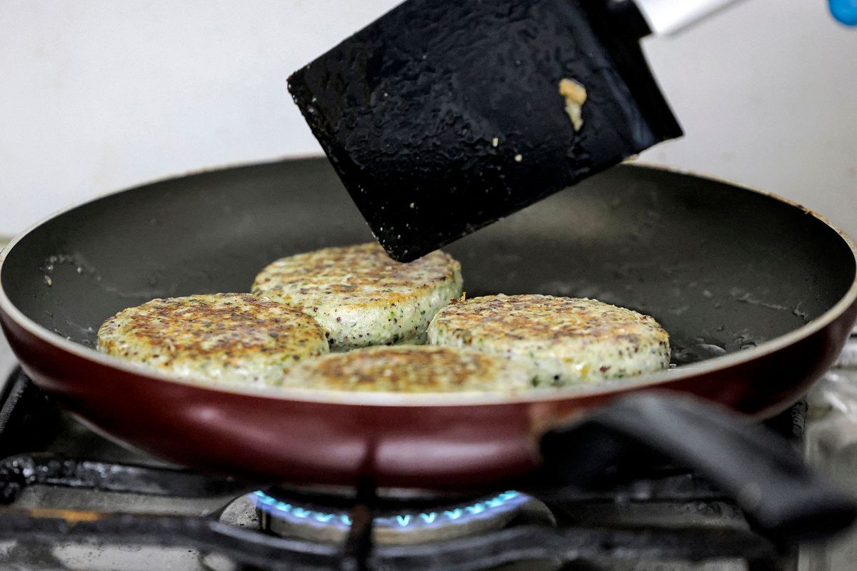 A worker cooks salicornia plant-based burger patties in a pan at a food processing plant in the Gulf emirate of Sharjah on June 8, 2022. - From desert farm to fork, the UAE is cultivating salicornia, a plant that grows in saline conditions, preparing for the future of agriculture in its arid climate. (Photo by Karim SAHIB / AFP)