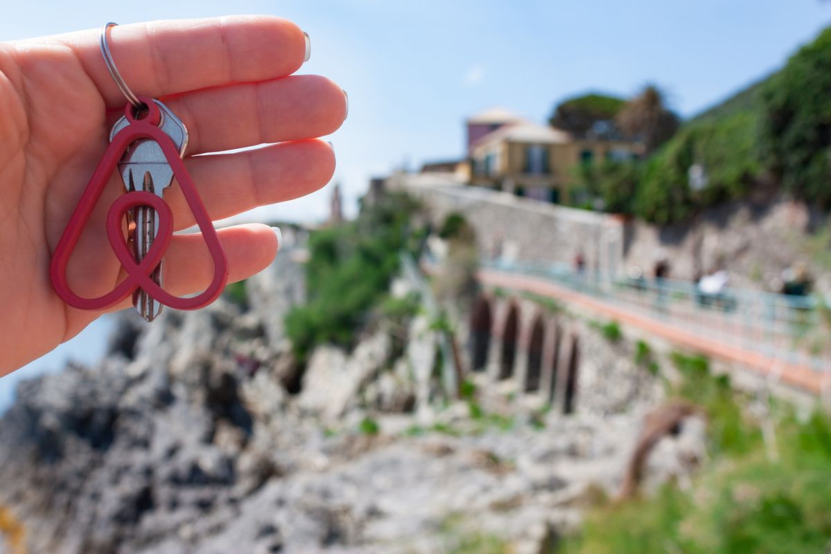 Genova, Italy. May, 2019. Woman holds the key with the logo of a popular company Airbnb.Travel around the world with Airbnb. Logo and the city on the background. Home concept. 