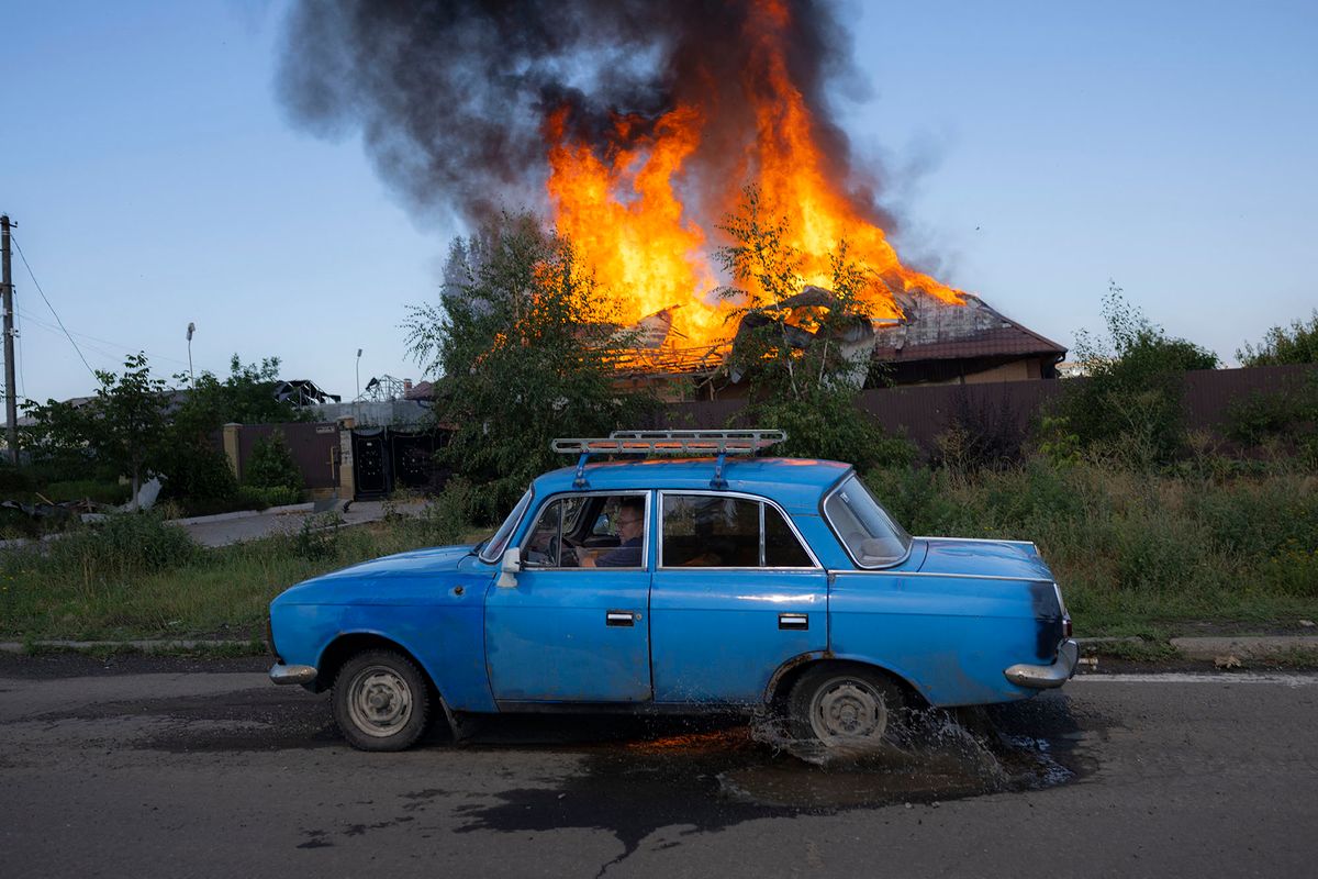 TOPSHOT - A Ukrainien man drives past a burning house hit by a shell in the outskirts of Bakhmut, Eastern Ukraine, on July 27, 2022, amid the Russian invasion of Ukraine. (Photo by BULENT KILIC / AFP)