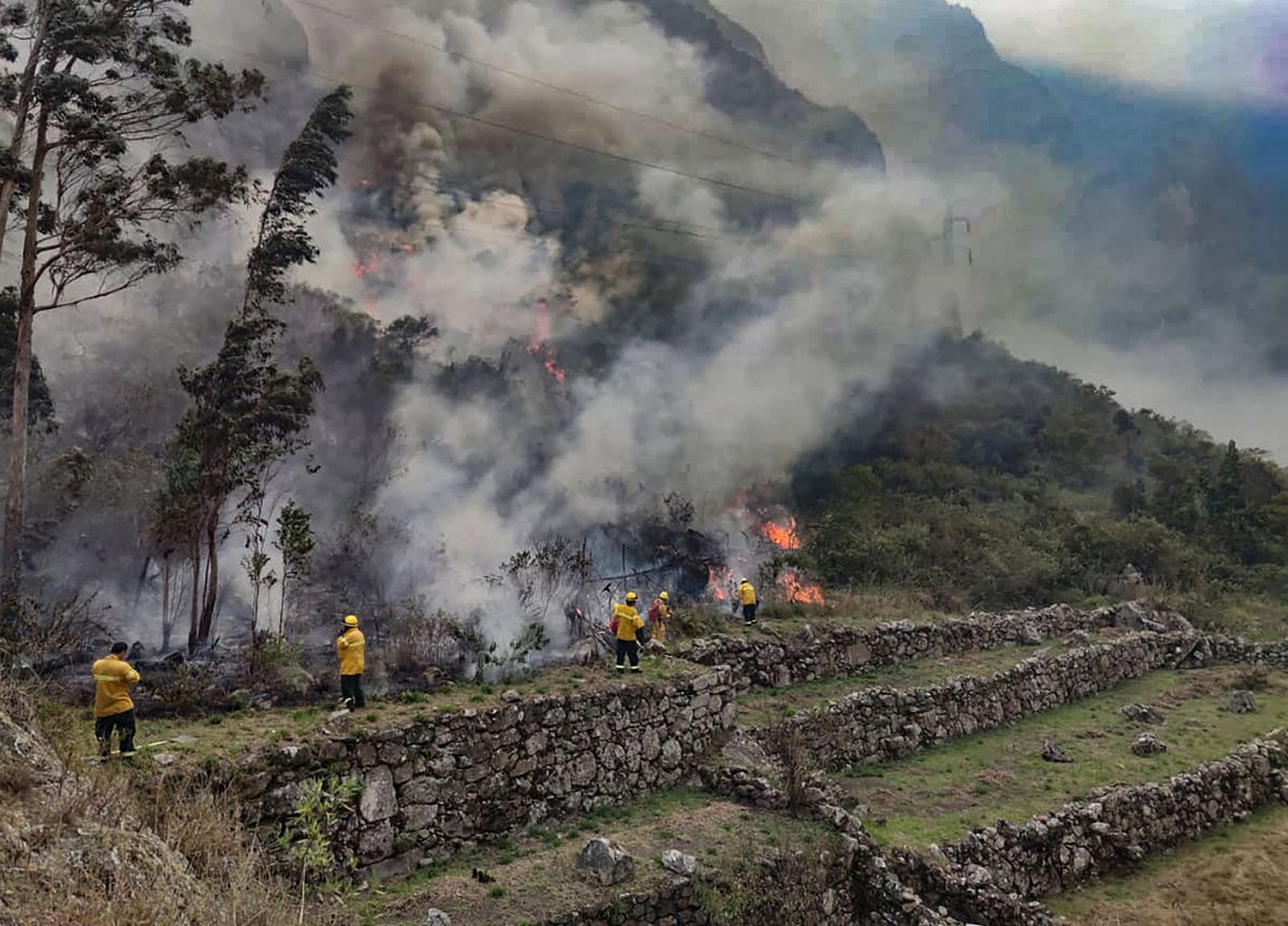 Handout picture released by the Municipality of Machu Picchu showing firemen working to put out a fire in the bush surrounding the ruins of Llamakancha, a sector in the archaeological site of Machu Picchu, the Inca jewel of Peru's travel industry, in the highlands close to the city of Cusco, on June 28, 2022. (Photo by Jesus TAPIA / Machu Picchu Municipality / AFP) / RESTRICTED TO EDITORIAL USE - MANDATORY CREDIT "AFP PHOTO / MACHU PICCHU MUNICIPALITY / JESUS TAPIA" - NO MARKETING - NO ADVERTISING CAMPAIGNS - DISTRIBUTED AS A SERVICE TO CLIENTS