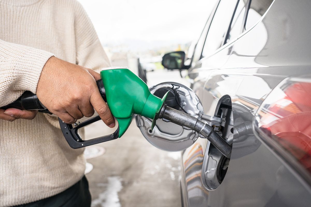 Hand refilling the car with fuel at the refuel station. Grey car at gas station being filled with fuel at New Zealand. Handle fuel nozzle to refuel. Vehicle fueling facility.