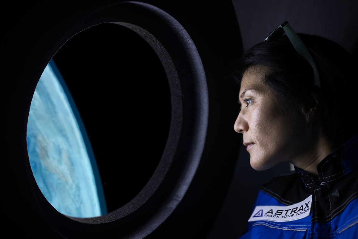 A female commercial space traveler looking at the earth through the window inside of the spaceship.