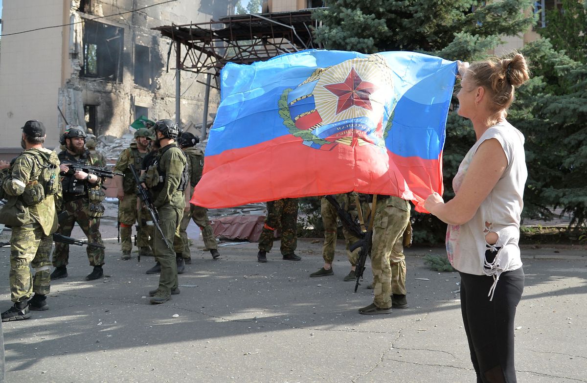 8228965 02.07.2022 A resident holds the flag of the LPR, donated by the soldiers of the 6th Platov Cossack Regiment at the administration building in Lisichansk, the Luhansk People's Republic. Viktor Antonyuk / Sputnik (Photo by Viktor Antonyuk / Sputnik / Sputnik via AFP)