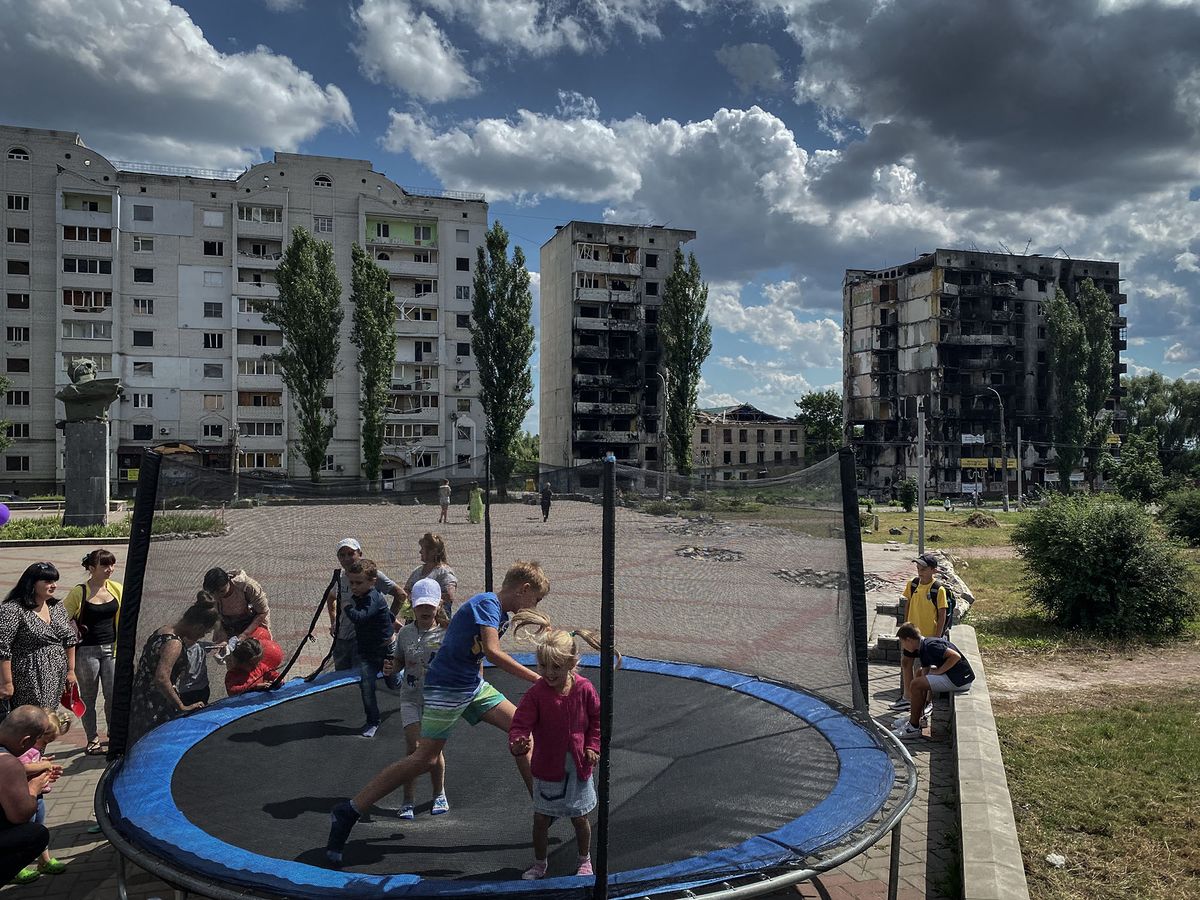 Children jump on a trampoline against the backdrop of destroyed buildings in Borodyanka, northwest of Kyiv on July 16, 2022. - Music teacher Oksana Shevchenko sits near a small pile of twisted metal and cement, the only break in a flat expanse of desolate, empty terrain. It is all that is left of the music school where she worked for 30 years, pulverised when the Russian army took over her home town of Borodyanka, an hour's drive northwest of Ukraine's capital, Kyiv. "Look, just burned down wasteland," the 53-year-old says, visibly angry. "Soil and nothing else in this place of culture, where children used to study... This is the extermination of culture and Ukrainians by Russian occupiers." (Photo by Ionut IORDACHESCU / AFP)