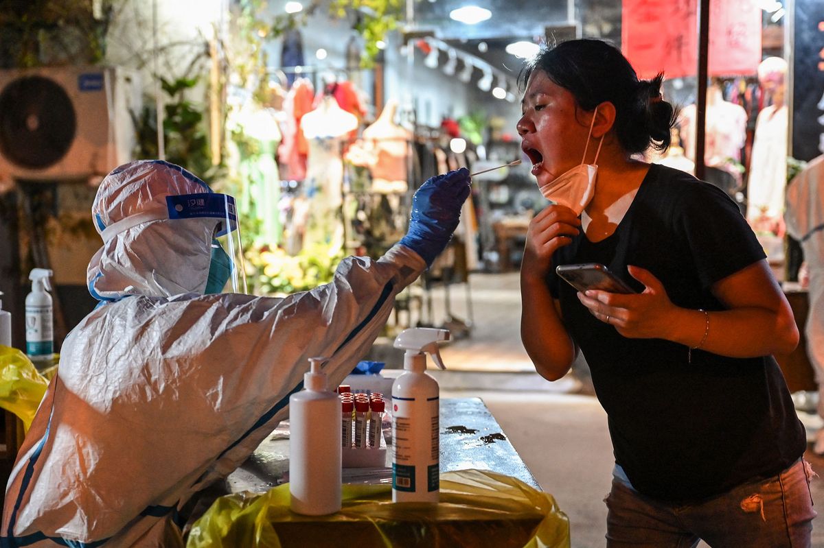 A health worker takes a swab sample from a woman to test for the Covid-19 coronavirus in the Huangpu district of Shanghai on July 12, 2022. (Photo by Hector RETAMAL / AFP)