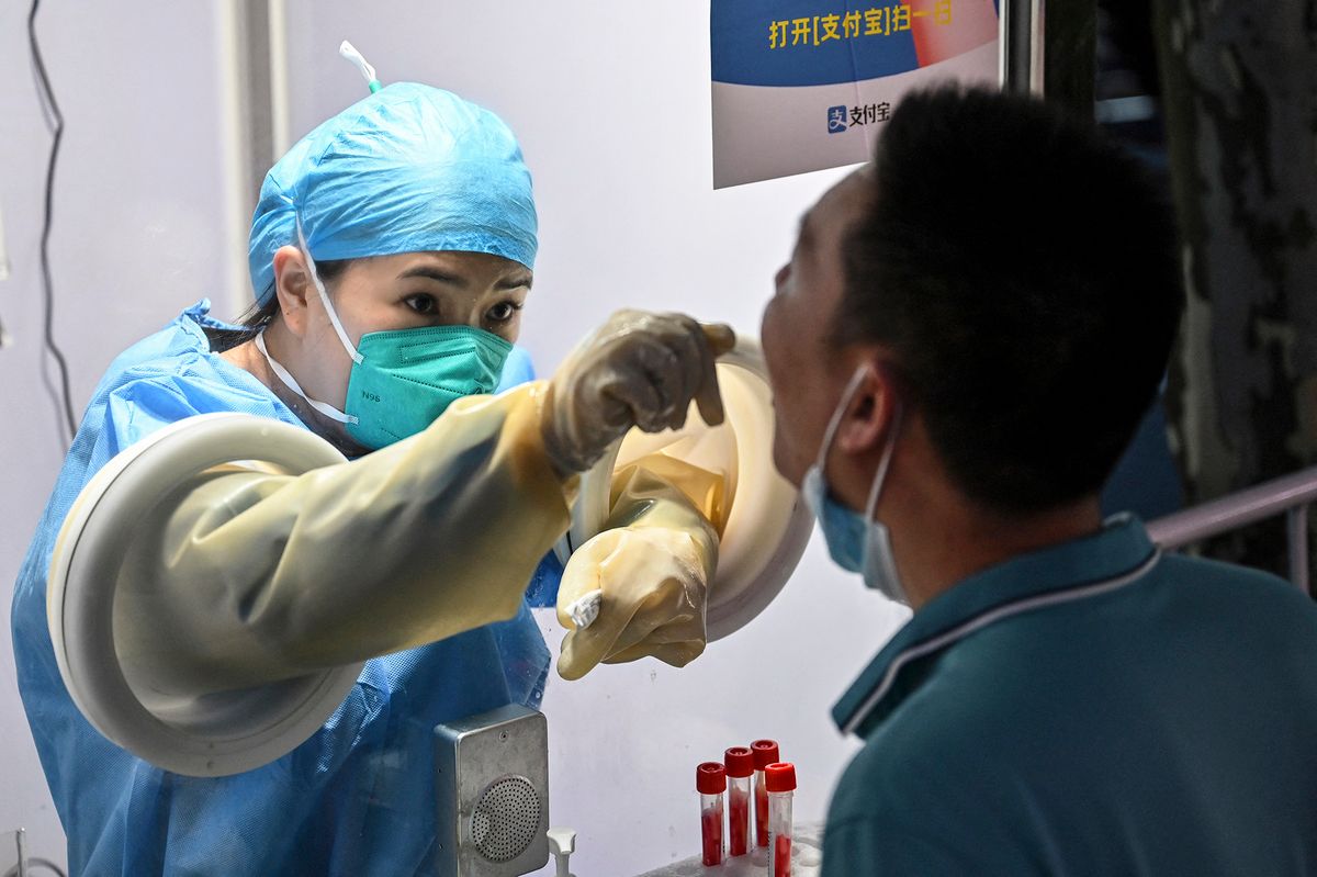 A health worker takes a swab sample from a man to test for the Covid-19 coronavirus in the Jing'an district of Shanghai on July 5, 2022. (Photo by Hector RETAMAL / AFP)