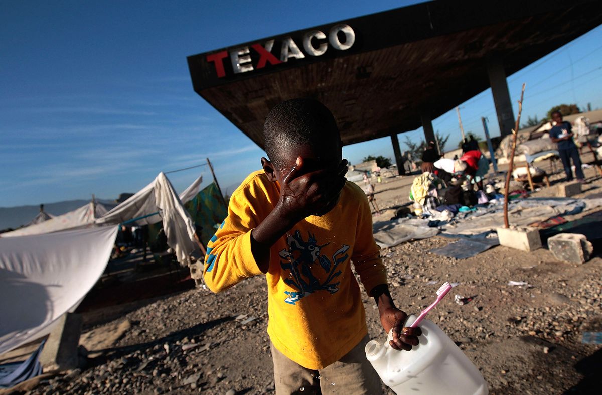 PORT-AU-PRINCE, HAITI - JANUARY 16:  A Haitian child washes his face at a makeshift camp at a fuel station January 16, 2010 on the edge of Port-au-Prince, Haiti. Haiti is trying to recover from a powerful 7.0-strong earthquake on January 12 that struck and devastated the city while displacing millions and killing thousands.   (Photo by Chris Hondros/Getty Images)