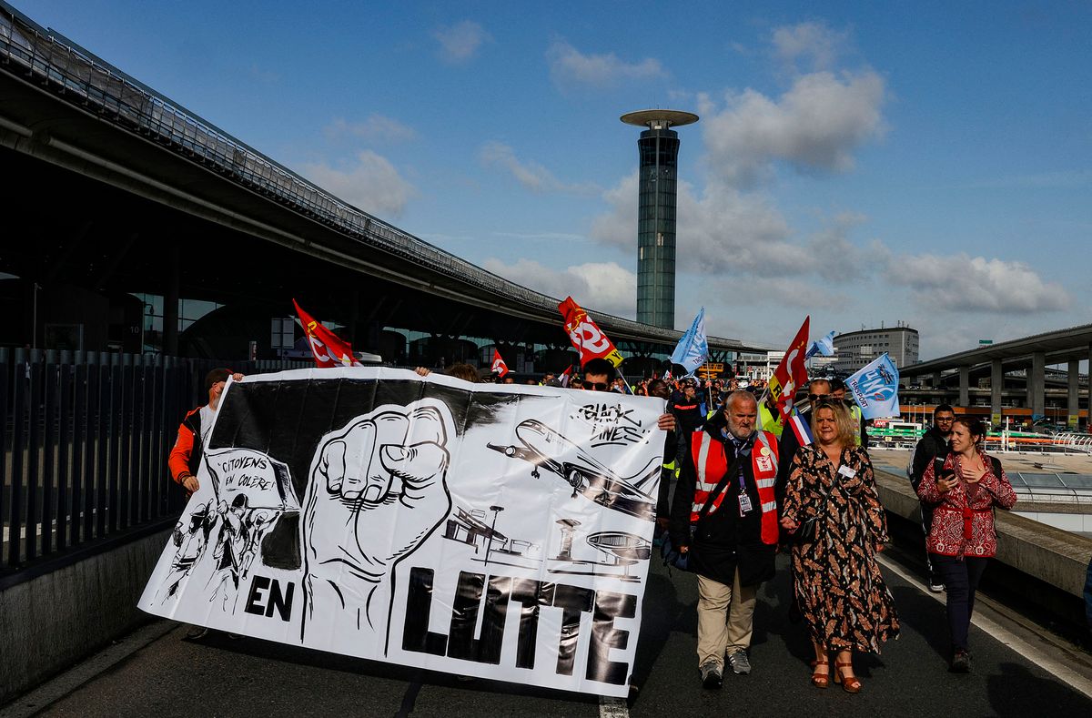 Paris Charles de Gaulle airport employees march with trade union flags as they stage a strike to demand higher wages at Roissy Charles De Gaulle Airport, north of Paris, on June 9, 2022. - A quarter of flights are expected to be cancelled at the airport, according to the airport operator ADP. The strike comes as several European airports have struggled to handle passenger flows due to staff shortages as the travel industry bounces back from the Covid pandemic. (Photo by Geoffroy Van der Hasselt / AFP)