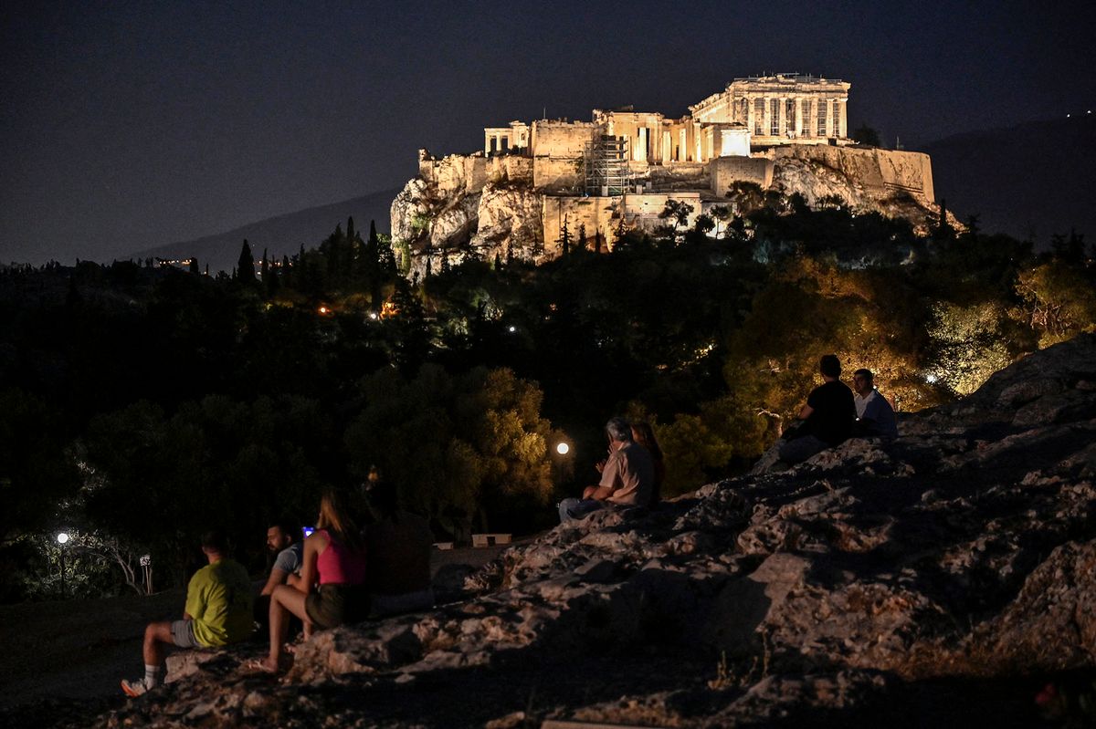 People sit on a hill facing the Ancient Acropolis in Athens on June 21, 2022. (Photo by Louisa GOULIAMAKI / AFP)