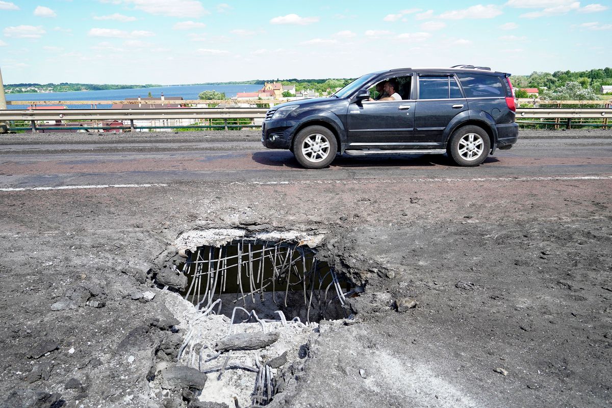 A picture taken on July 21, 2022 shows a car moving past a crater on Kherson's Antonovsky bridge across the Dnipro river caused by a Ukrainian rocket strike, amid the ongoing Russian military action in Ukraine. (Photo by STRINGER / AFP)