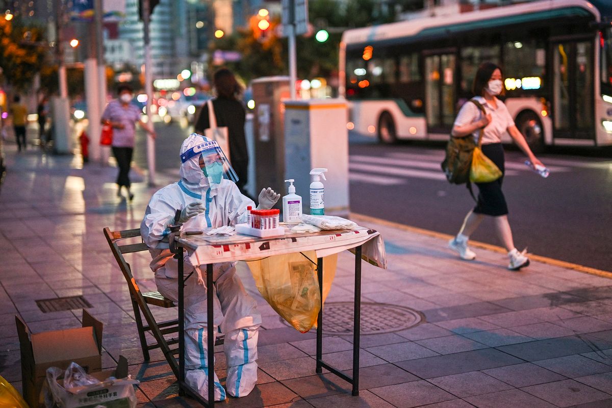 A health worker waits to test people for the Covid-19 coronavirus on a street next to a residential area in the Jing'an district of Shanghai on July 5, 2022. (Photo by Hector RETAMAL / AFP)