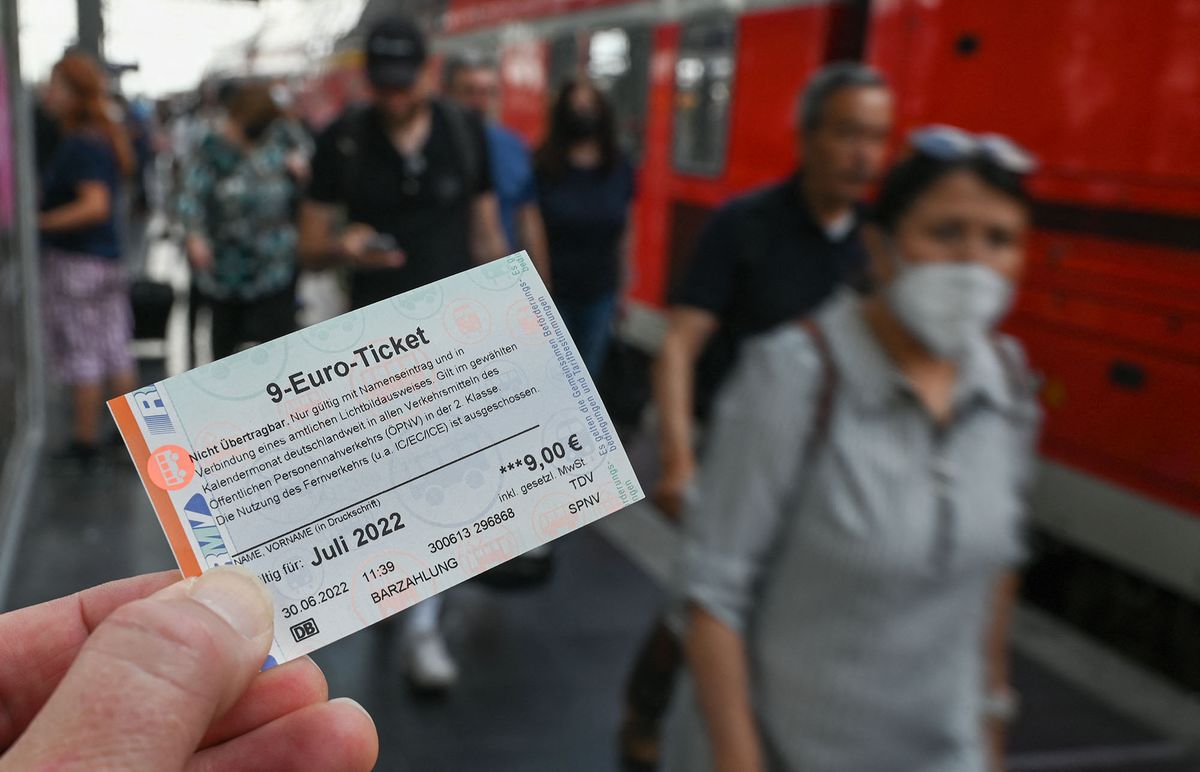 30 June 2022, Hessen, Frankfurt/Main: A 9-euro ticket for July 2022 is held up at the main train station as train passengers get off a regional train. For 9 euros a month throughout Germany - this offer has convinced many people. Initial data even suggests that car drivers will also benefit. Photo: Arne Dedert/dpa (Photo by ARNE DEDERT / DPA / dpa Picture-Alliance via AFP)