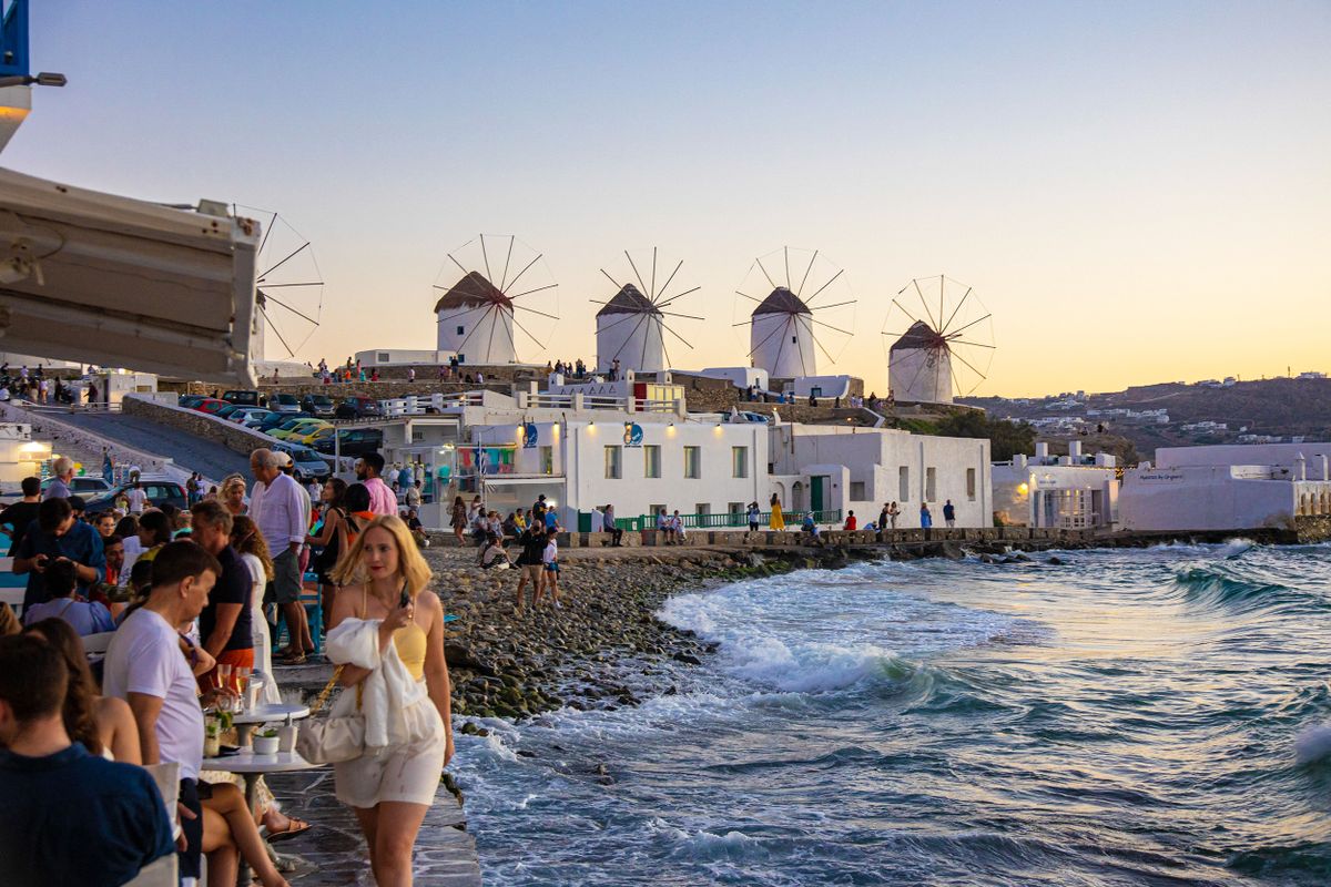 The iconic windmills of Mykonos island as seen from Little Venice with tourists at the bars, cafes and restaurants. Mykonos is an island in Greece in the Aegean sea. There are 16 windmills on the island, 5 of them above Chora, the main town in the island. The windmills were built in the 16th century from the Venetians but their constructions continued until the 20th century. Sunset with people at the windmills in Mykonos. Tourists enjoy a beautiful sunset during the magic hour at Mykonos island in Greece. The Greek island of Myconos is a popular glamorous Mediterranean travel destination for holidays in the Cyclades, Aegean Sea with the iconic whitewashed buildings, the sandy beaches and famous party at the beach bars. The tourism and travel industry had a negative impact in the business and local economy sector due to the Covid-19 Coronavirus pandemic. Mykonos island, Greece(Photo by Nicolas Economou/NurPhoto) (Photo by Nicolas Economou / NurPhoto / NurPhoto via AFP)